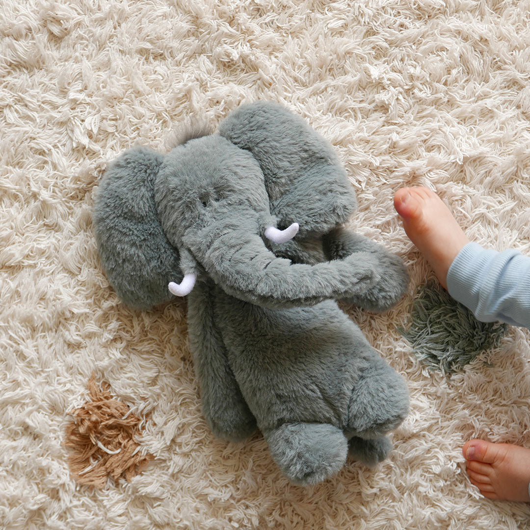 Elephant teddy lying on rug next to a baby's feet